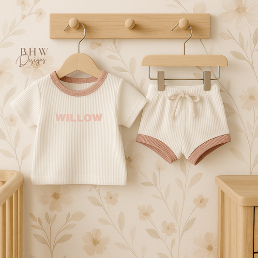 White ribbed Baby outfit with 'WILLOW' on the front in baby pink hanging in a nursery