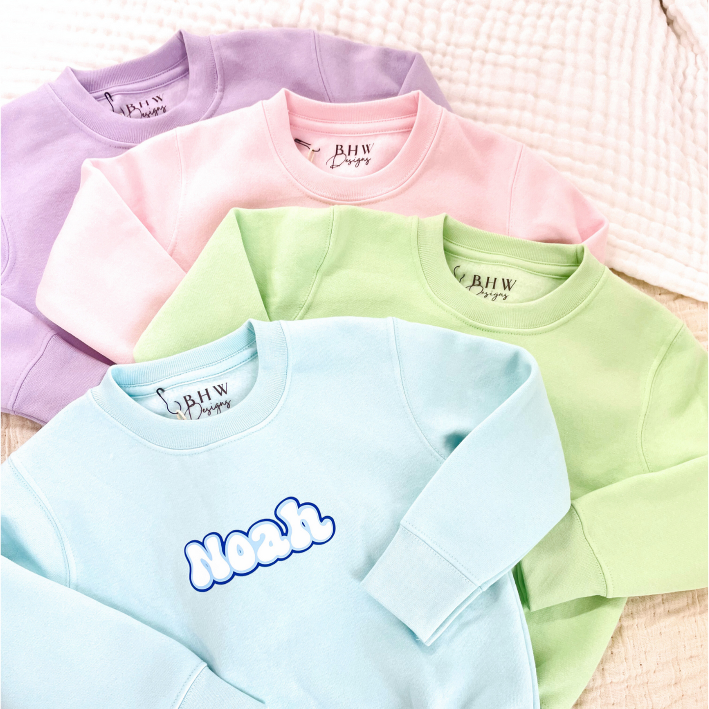 Four pastel-colored sweatshirts with 'BHW' branding on a textured surface.