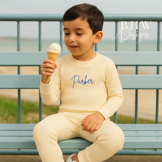 Child wearing a cream outfit with 'Parker' printed on it, sitting on a bench and eating an ice cream.