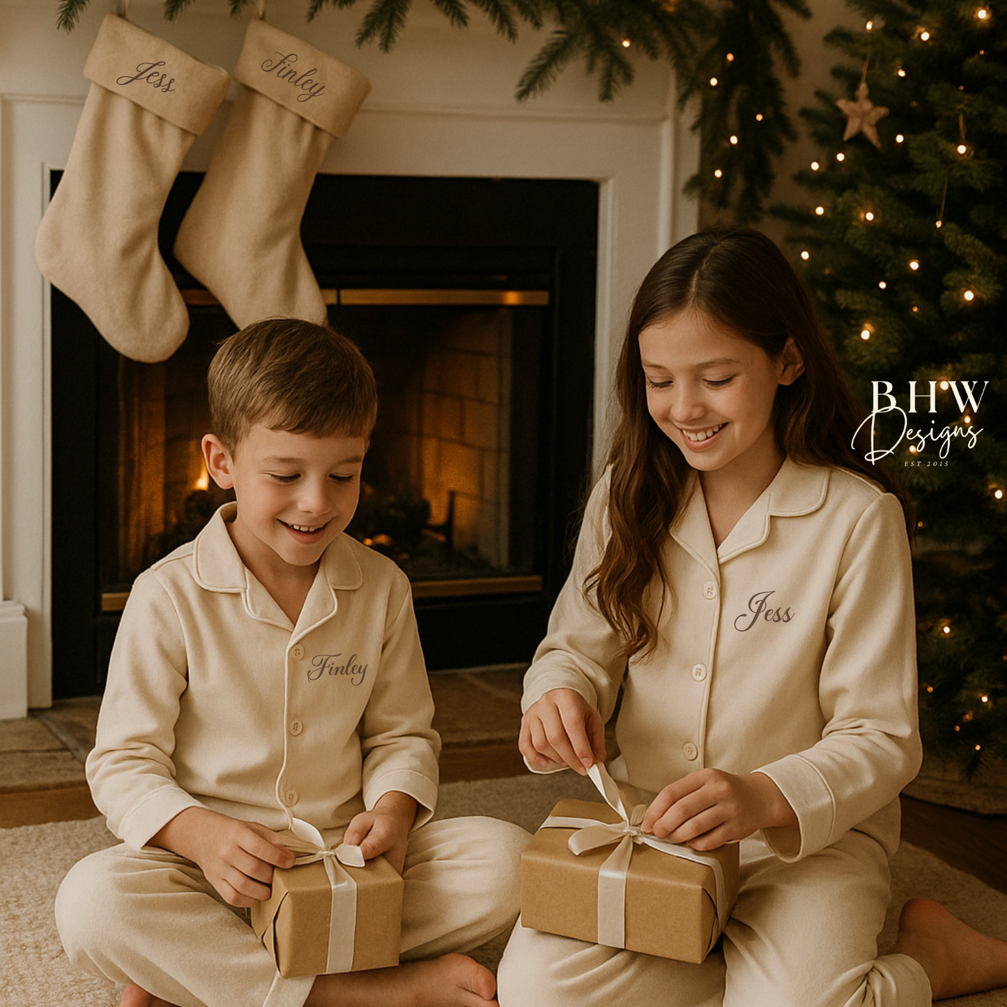 Two children in matching personalised beige pyjamas opening Christmas presents in front of a fireplace with personalised beige stockings hanging on the fireplace