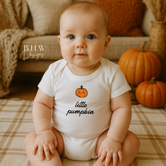 Baby wearing a 'little pumpkin' onesie sitting on a plaid blanket with pumpkins in the background.