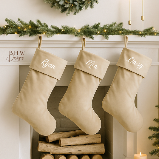 Three personalised beige Christmas stockings hanging above a fireplace with a wreath and candles in the background.