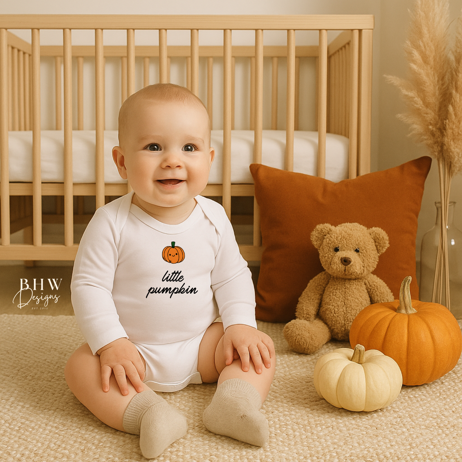 Baby wearing a 'little pumpkin' onesie sitting on the floor with pumpkins and a teddy bear.