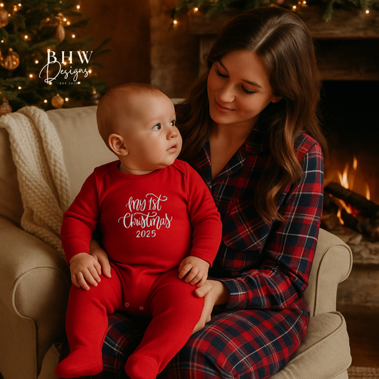Woman and baby in red 'My 1st Christmas 2025' outfit sitting on a couch with a fireplace in the background.