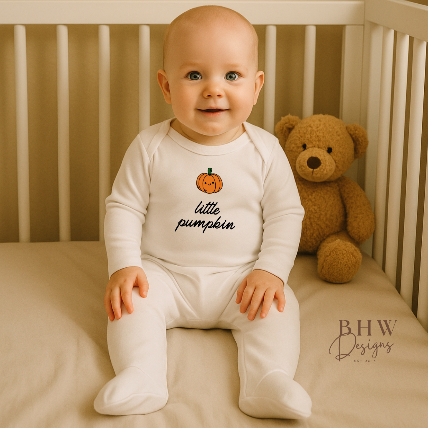 Baby sitting in a crib wearing a 'little pumpkin' onesie with a teddy bear in the background.