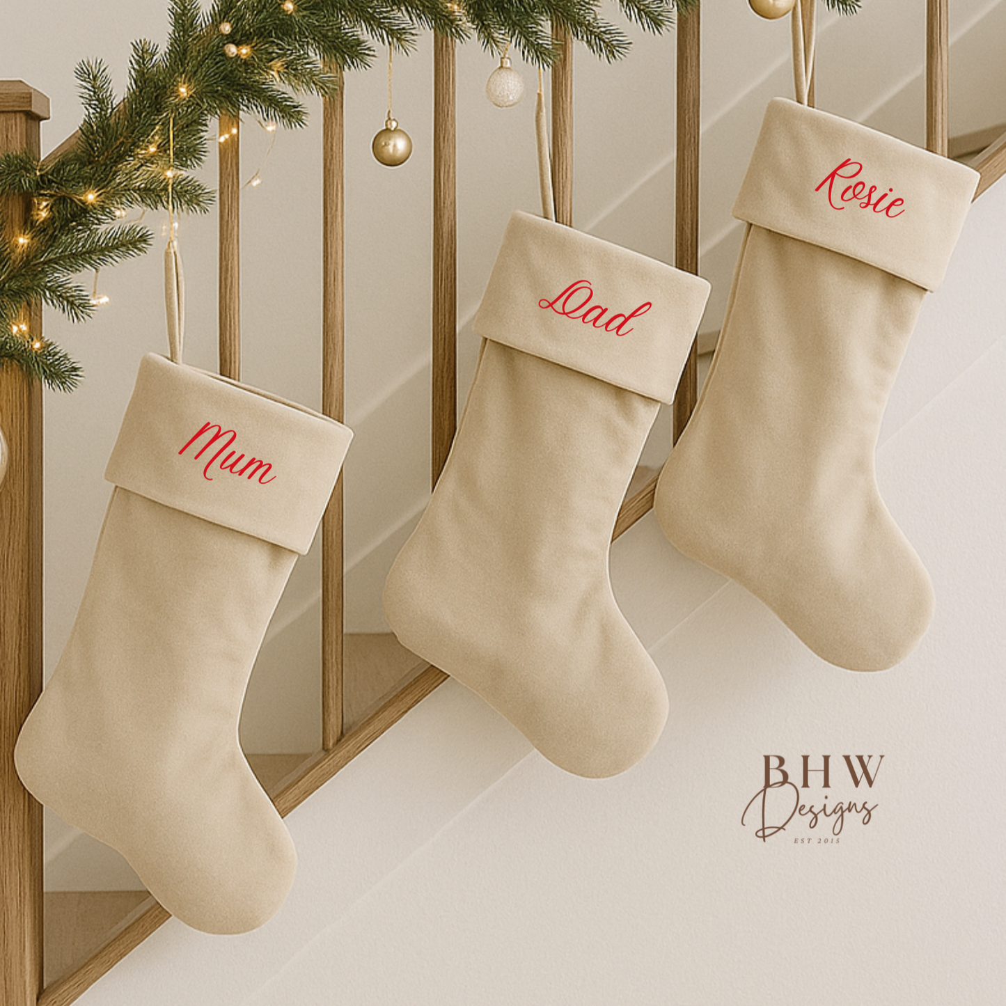 Three beige stockings with personalised names hanging on a staircase decorated with Christmas lights and garlands.