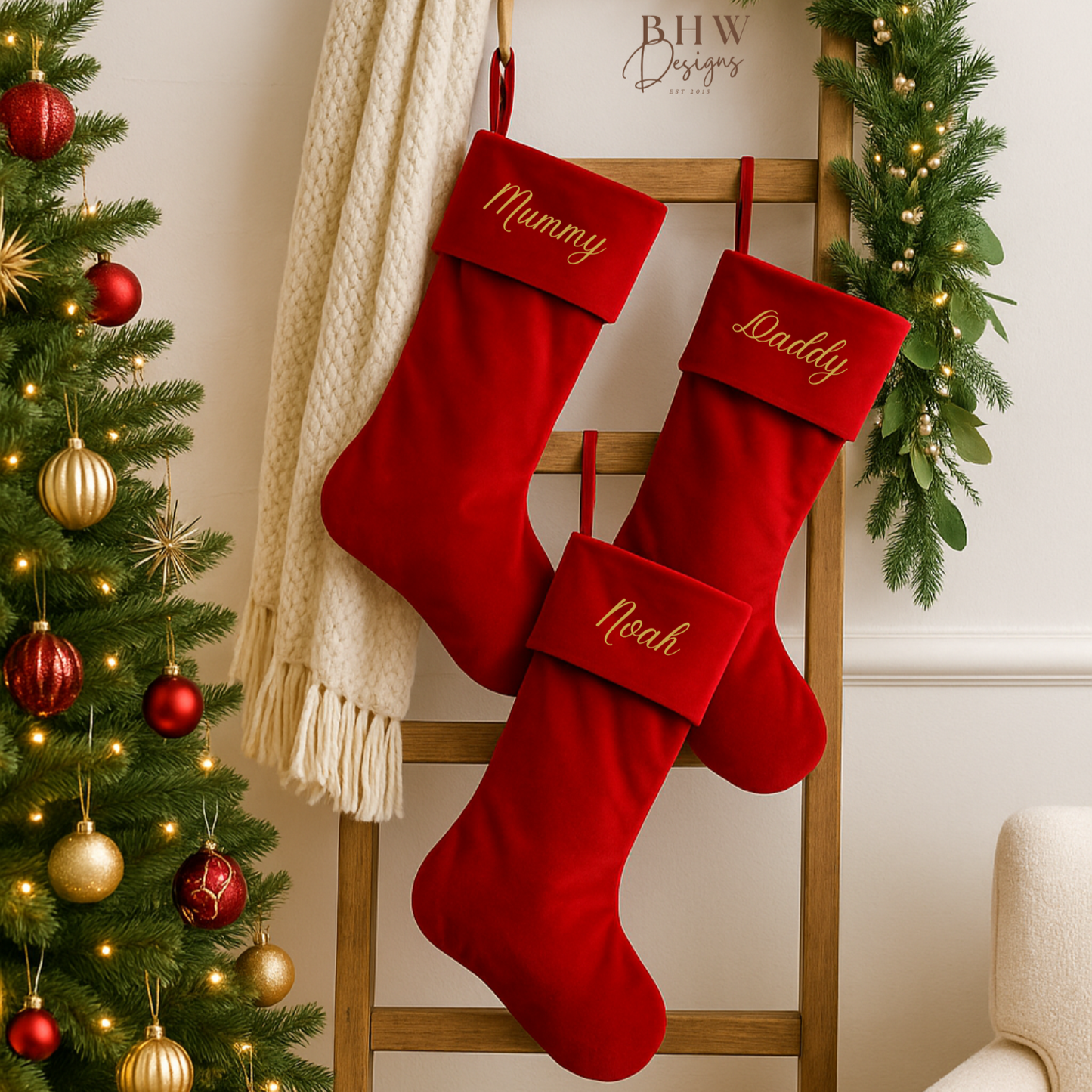 Red personalised Christmas stockings with embroidered names on a wooden ladder next to a decorated tree.