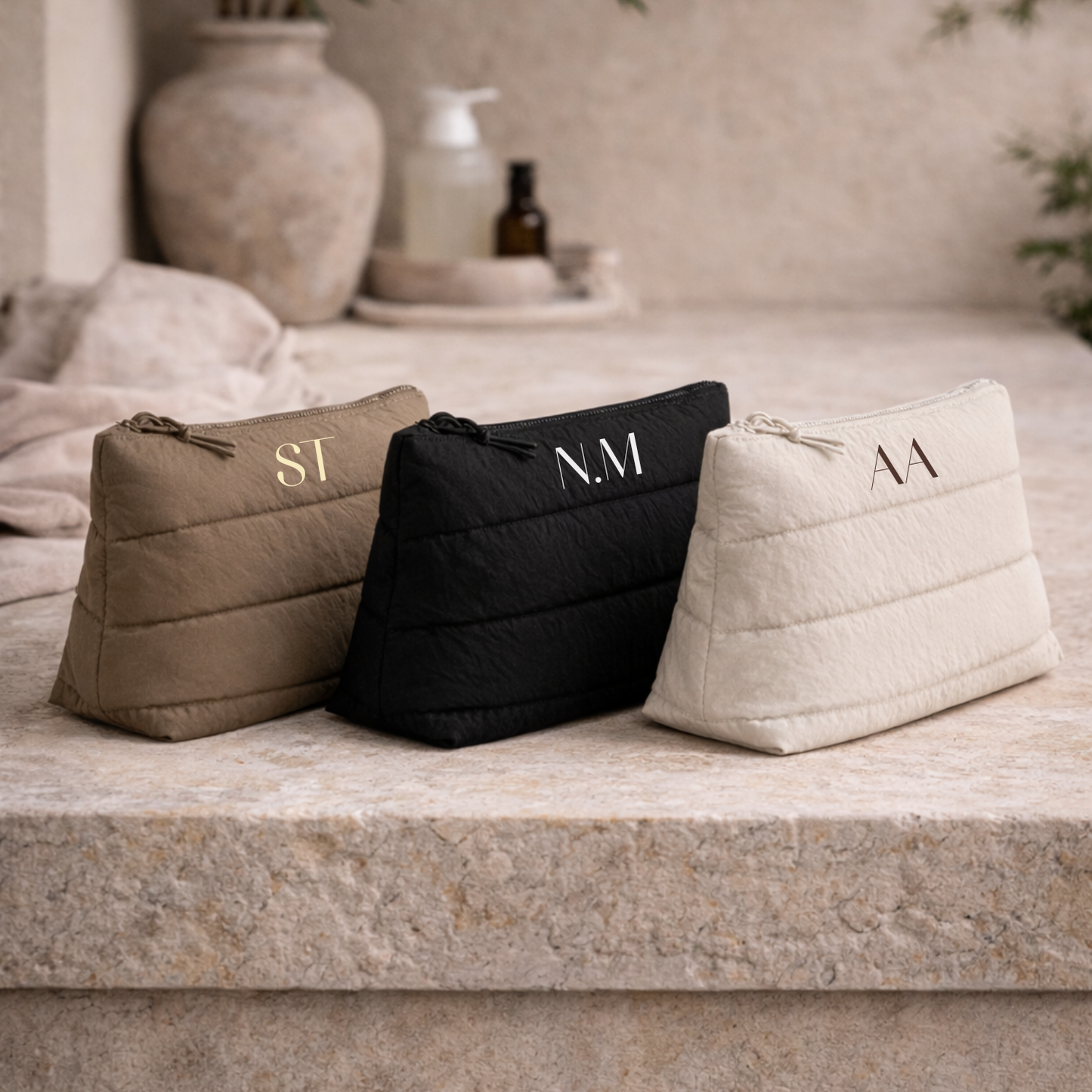 Three cosmetic bags with monogram initials on a stone surface.