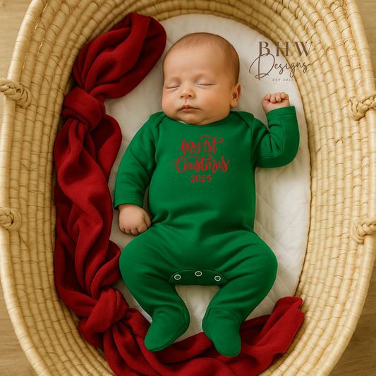 Newborn baby in a green onesie with My first christmas in red, lying on a textured surface with red fabric.