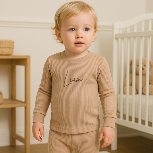 Child wearing a beige ribbed outfit with 'Liam' printed on it, standing in a nursery.