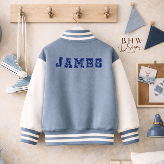 Dusky blue and white varsity jacket with 'JAMES' on the back, hanging on a wooden coat rack.