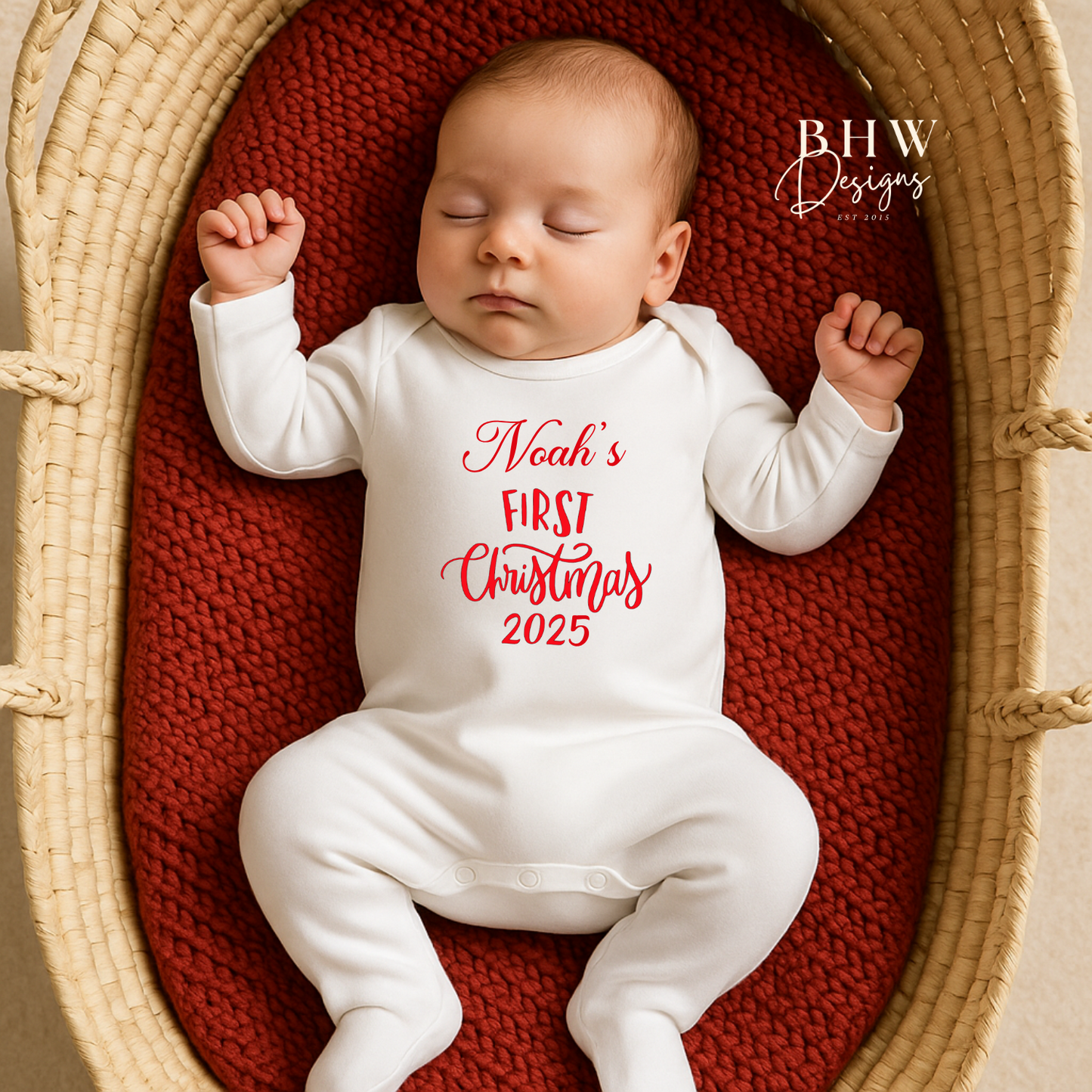 Baby in a white onesie with 'Noah's First Christmas 2025' text,in red lying in a woven basket.