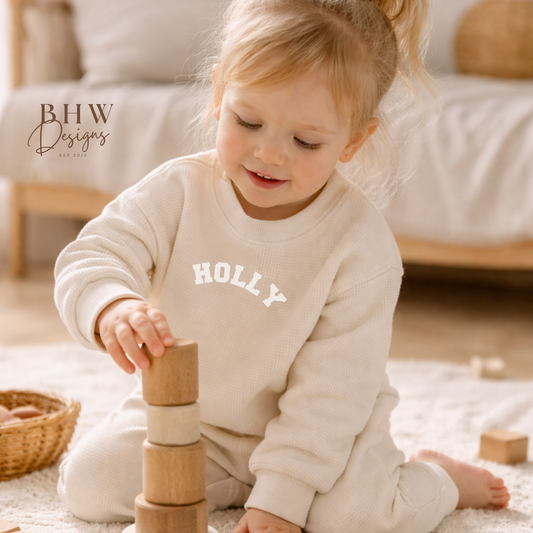 Child in a cream waffle personalised outfit playing with wooden blocks in a cozy room