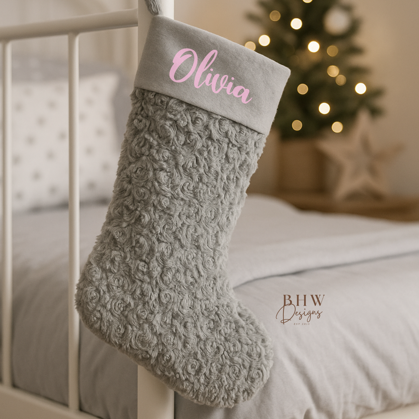 Grey textured Christmas stocking with 'Olivia' on it, hanging on a bed with a decorated tree in the background.