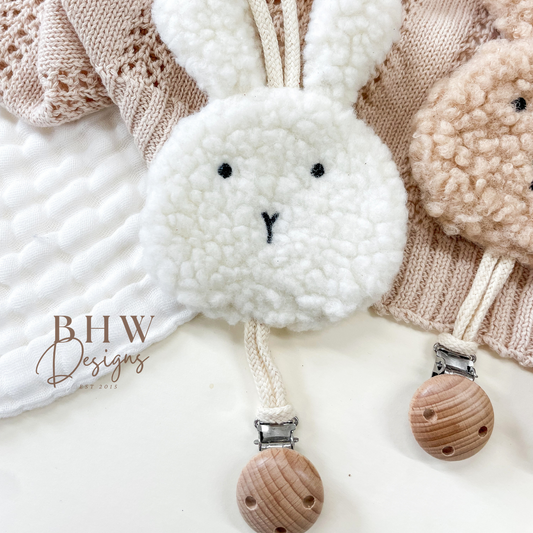White bunny-shaped pacifier clip with wooden CLIP on a textured blanket
