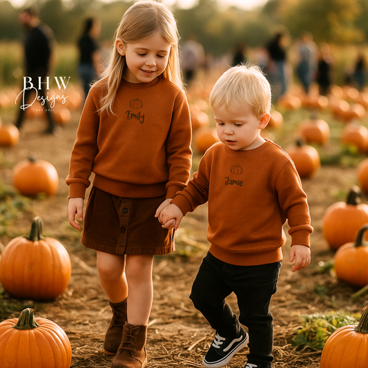Two children in matching personalised rust orange sweatshirts walking through a pumpkin patch.