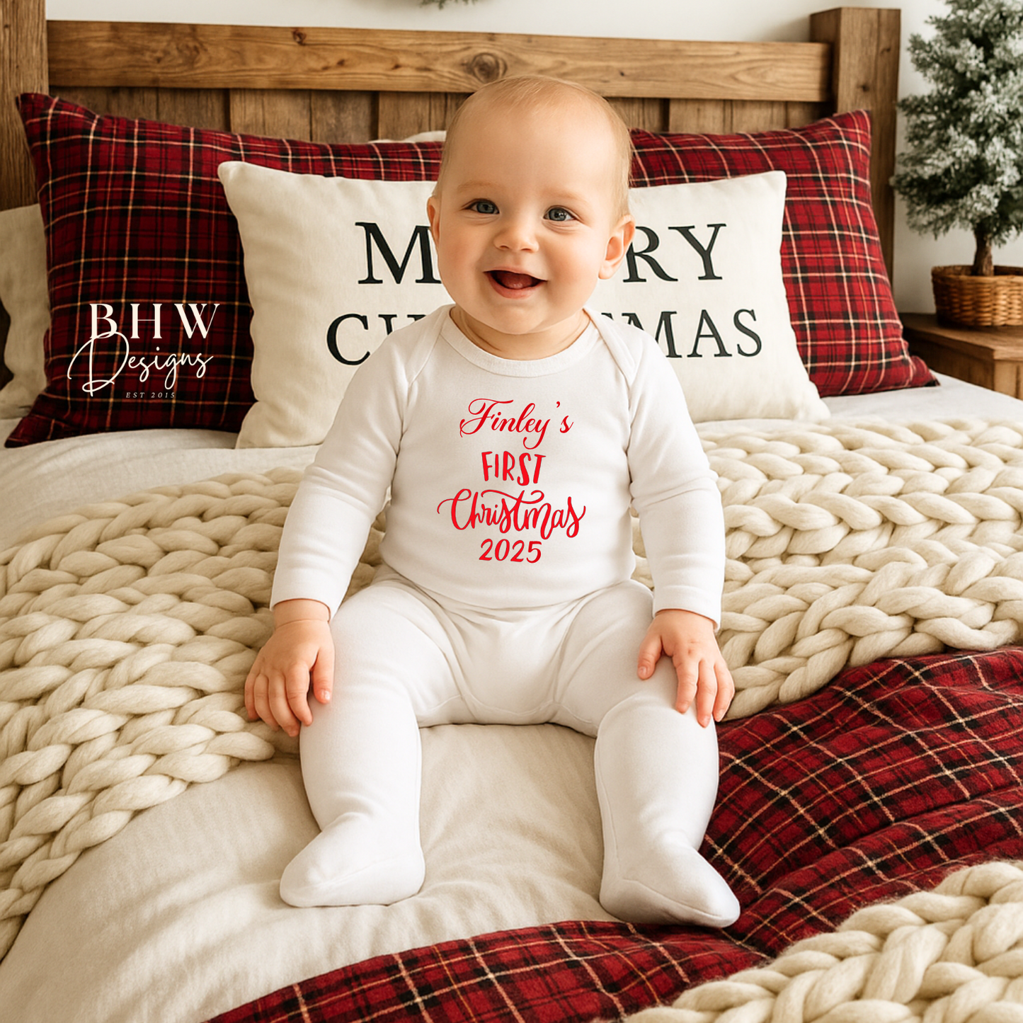 Baby wearing a 'Finley's First Christmas' onesie sitting on a bed with festive pillows and decorations.