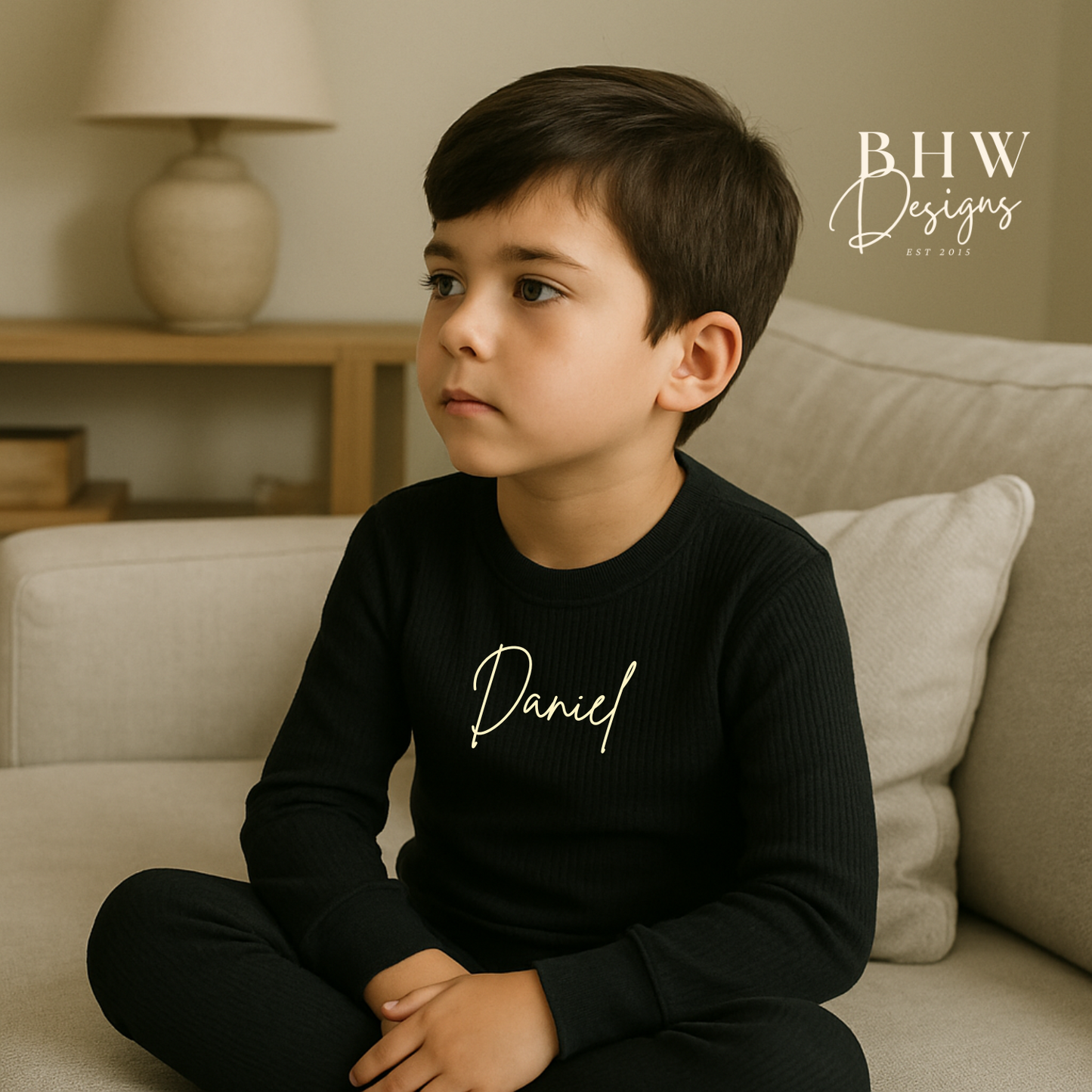 Child wearing a ribbed black outfit with 'Daniel' printed on it, sitting on a couch in a home setting.