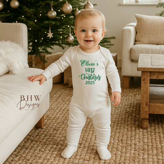 Baby in a 'First Christmas' onesie standing in a living room with a decorated tree.