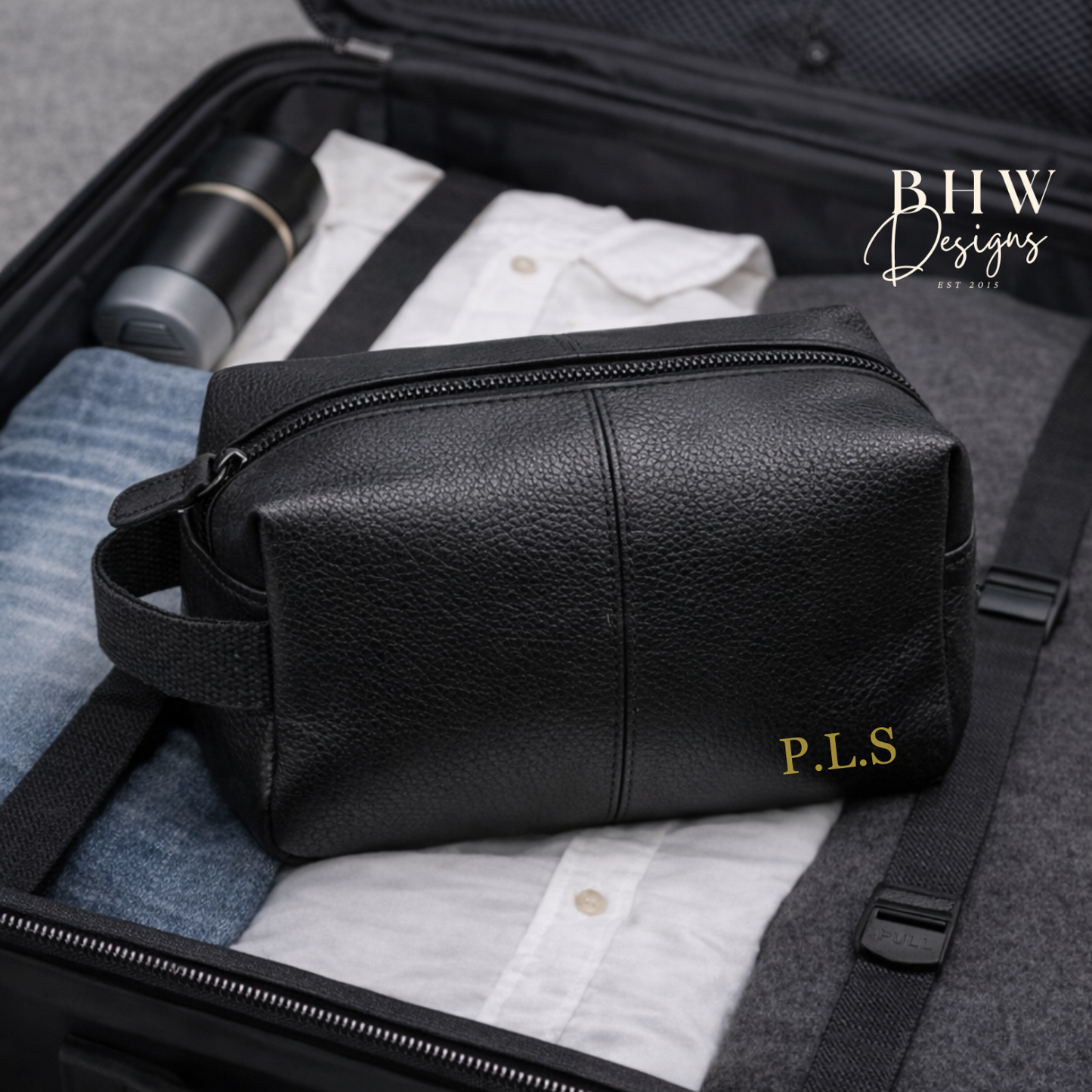 Black leather toiletry bag with 'P.L.S.' monogram inside an open suitcase.