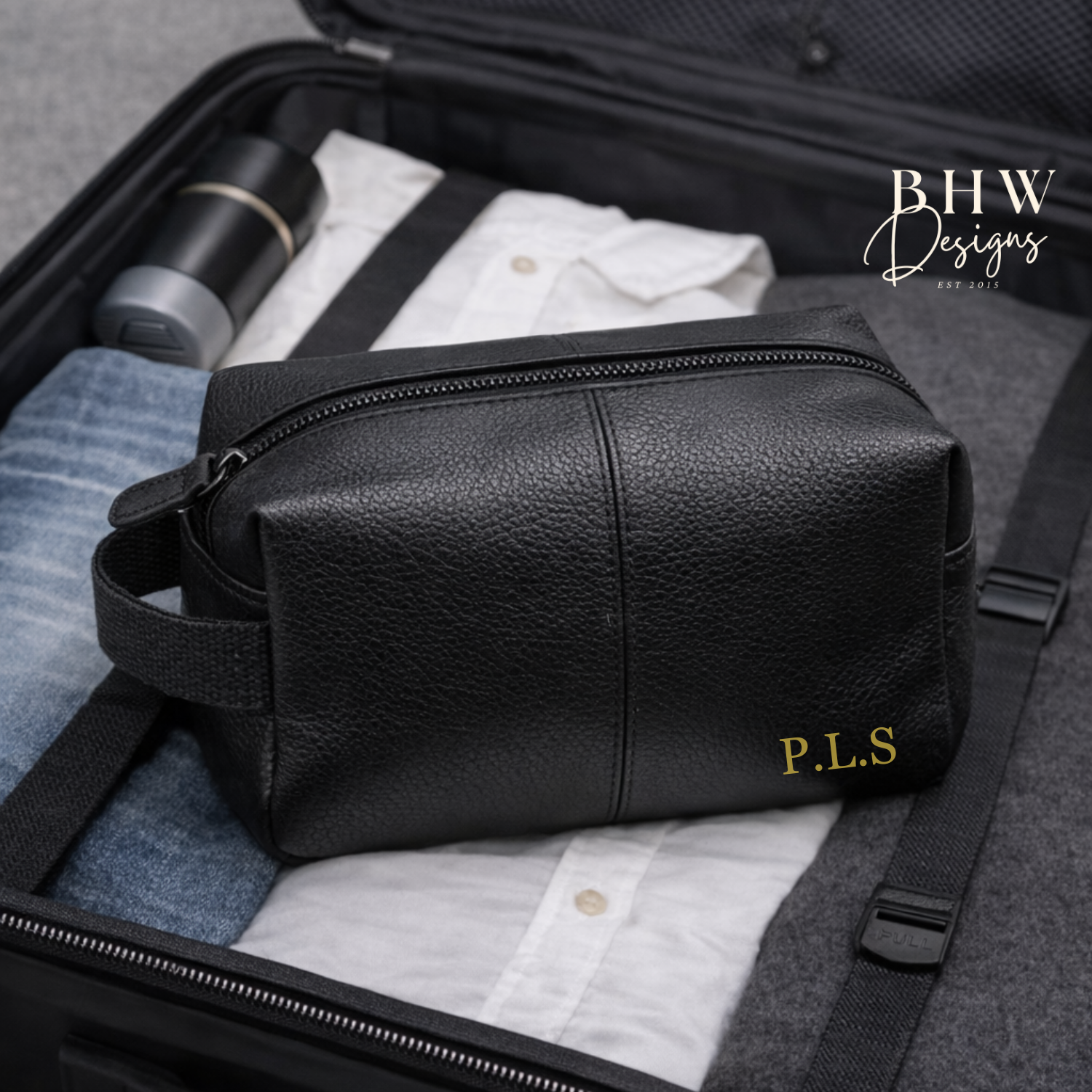 Black leather toiletry bag with 'P.L.S.' monogram inside an open suitcase.