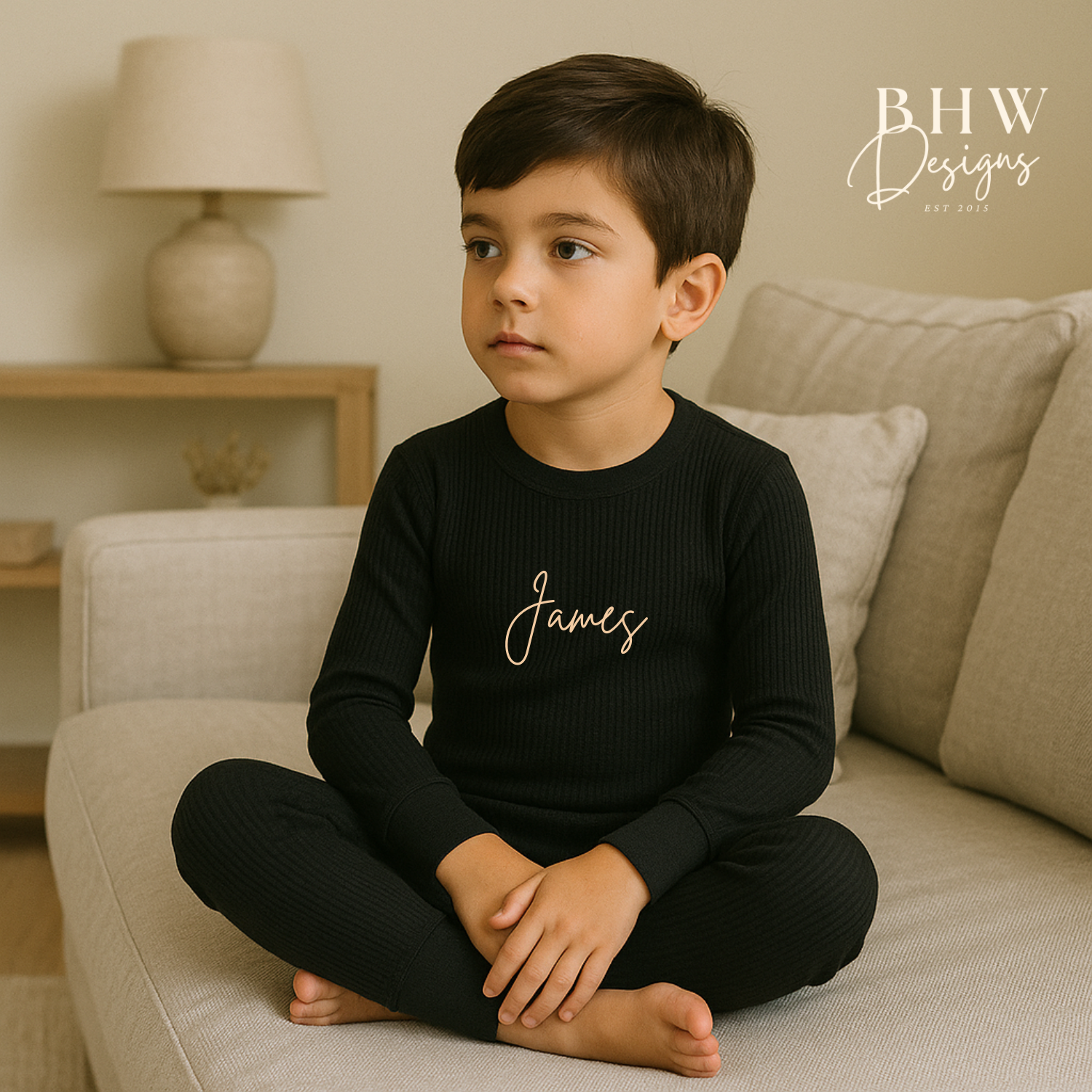 Child wearing a ribbed black outfit with 'James' printed on it, sitting on a couch.