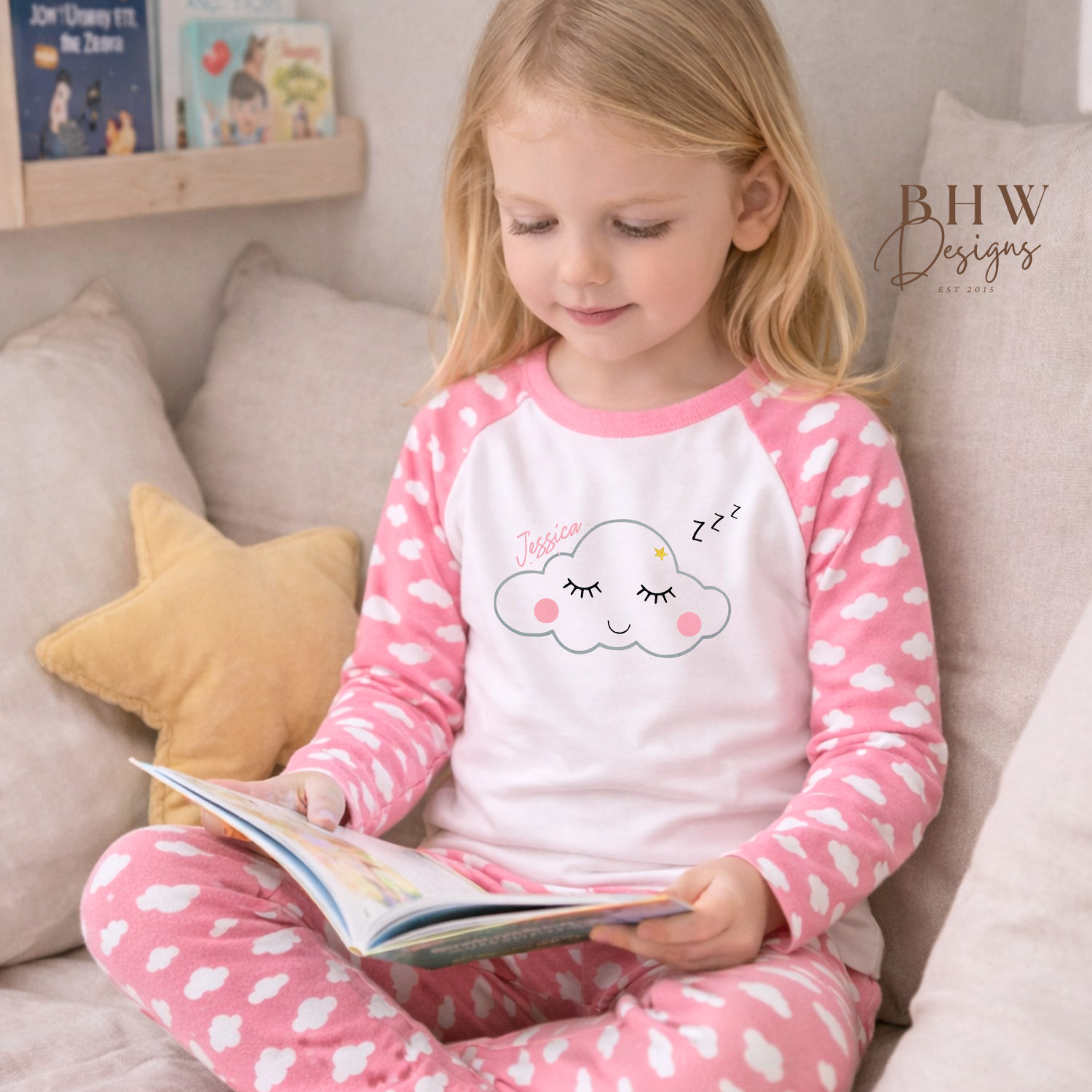 Child in pink and white cloud print pyjamas reading a book on a couch.