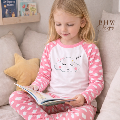Child in pink and white cloud print pyjamas reading a book on a couch.