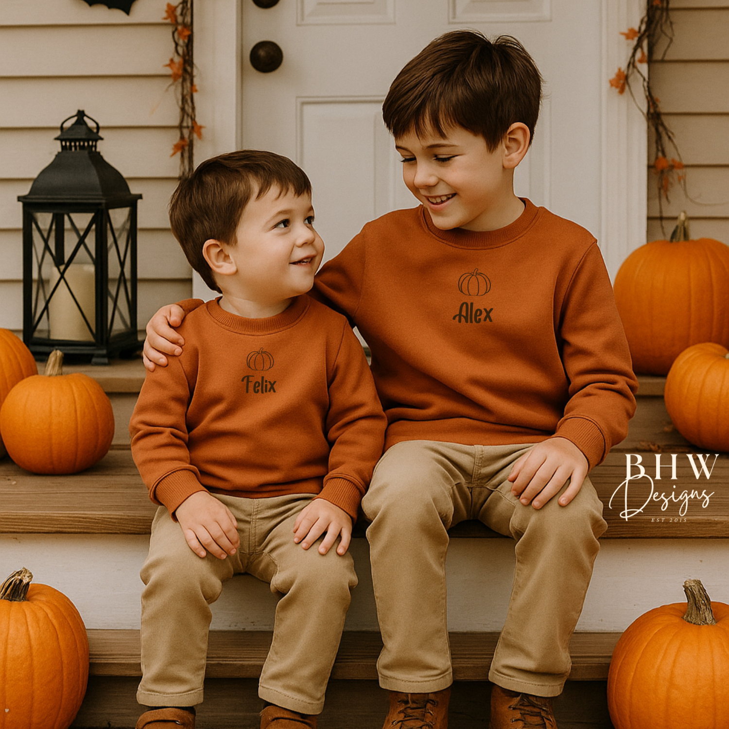 Two children wearing matching rust orange sweatshirts sitting on steps with pumpkins and Halloween decorations around.
