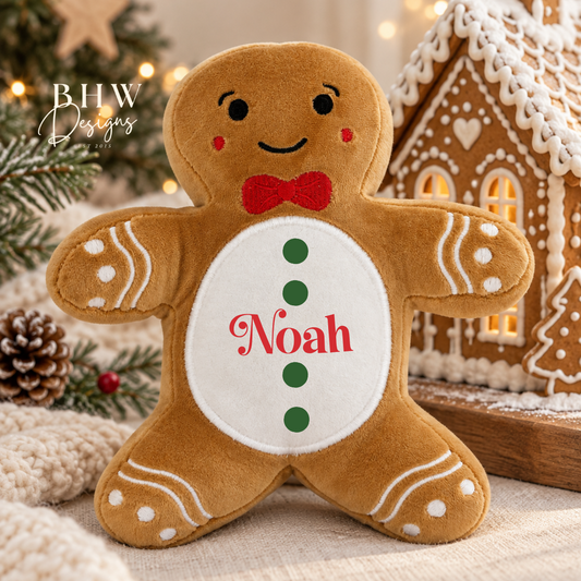 A personalized gingerbread man plush toy with a white belly patch featuring the name 'Noah' in red and green buttons, set against a cozy Christmas background with a gingerbread house and pine branches.