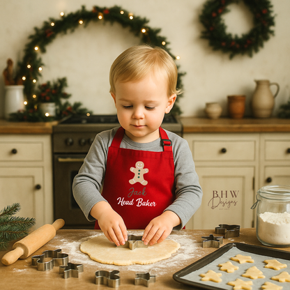Child in a red apron personalised with Jack and with 'Head Baker' text, making cookies in a kitchen decorated for Christmas.