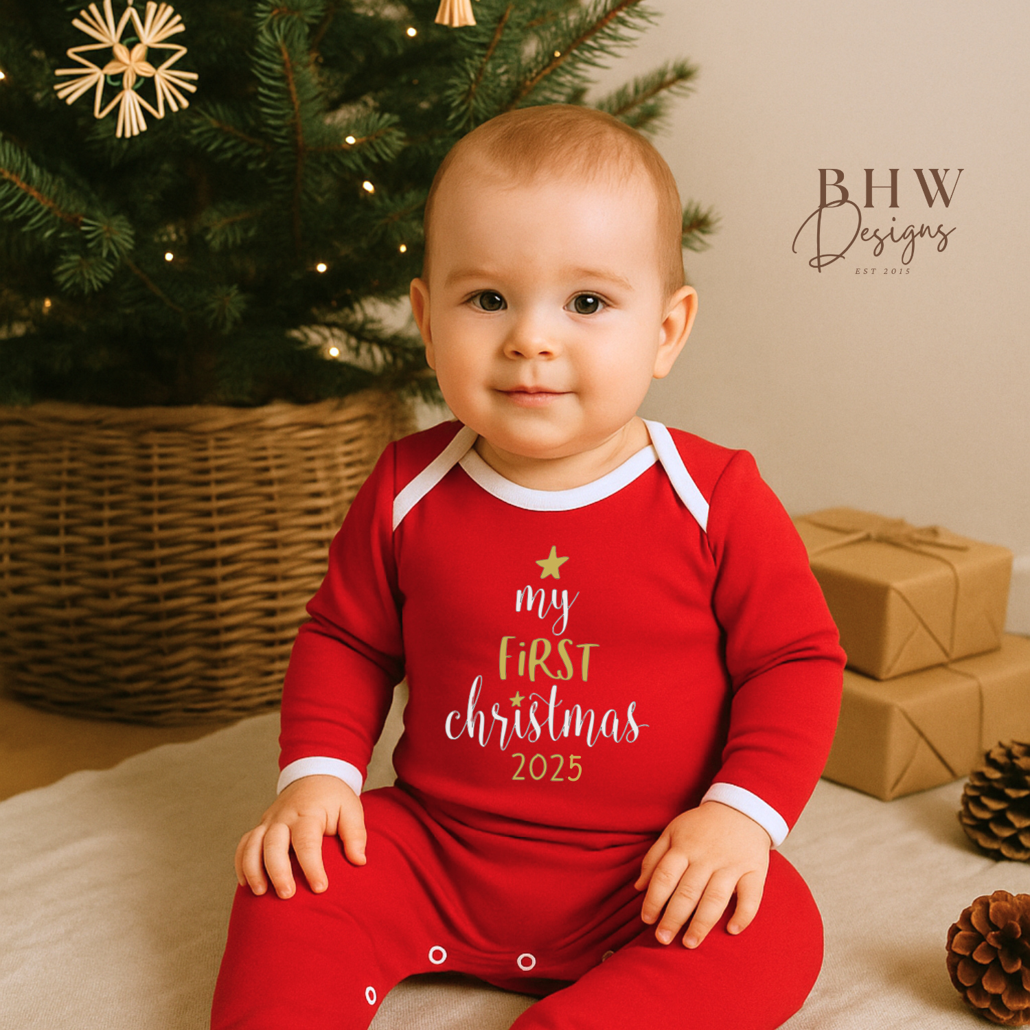 Baby wearing a red 'my first Christmas 2025' outfit in front of a Christmas tree and presents.