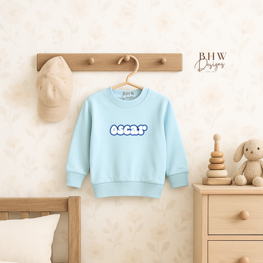 Light blue sweatshirt personalised with text on a hanger in a child's room.