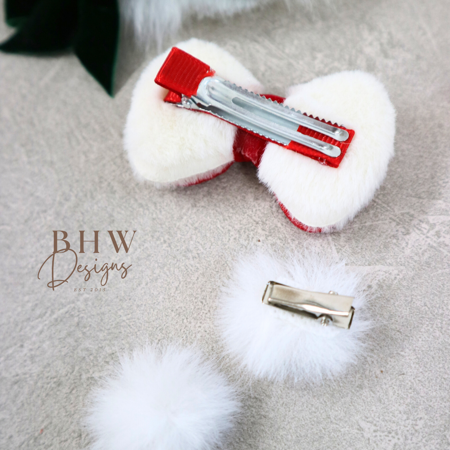 White fluffy hair bow with red center and silver clip on a grey surface,.