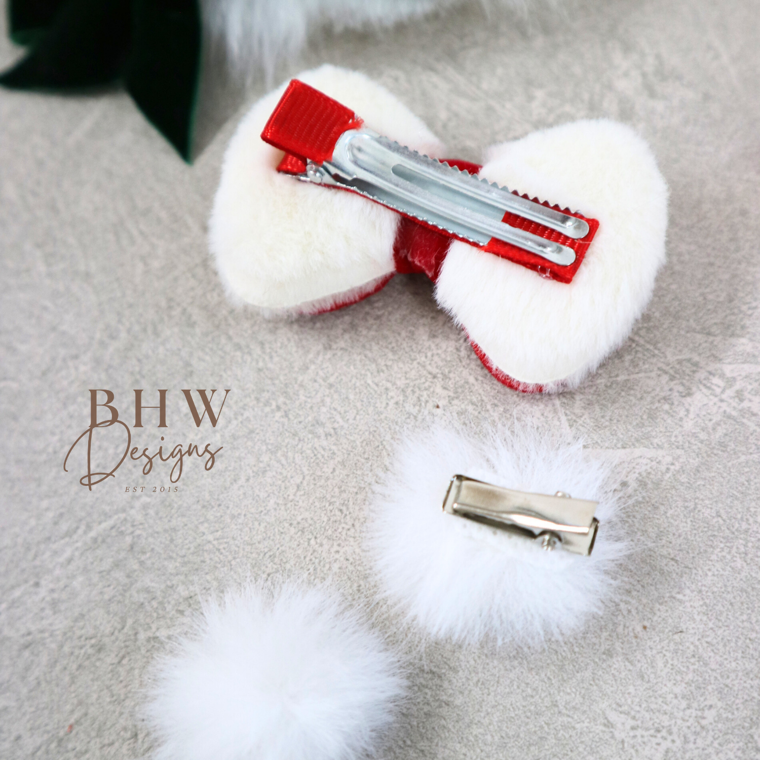 White fluffy hair bow with red center and silver clip on a grey surface,.