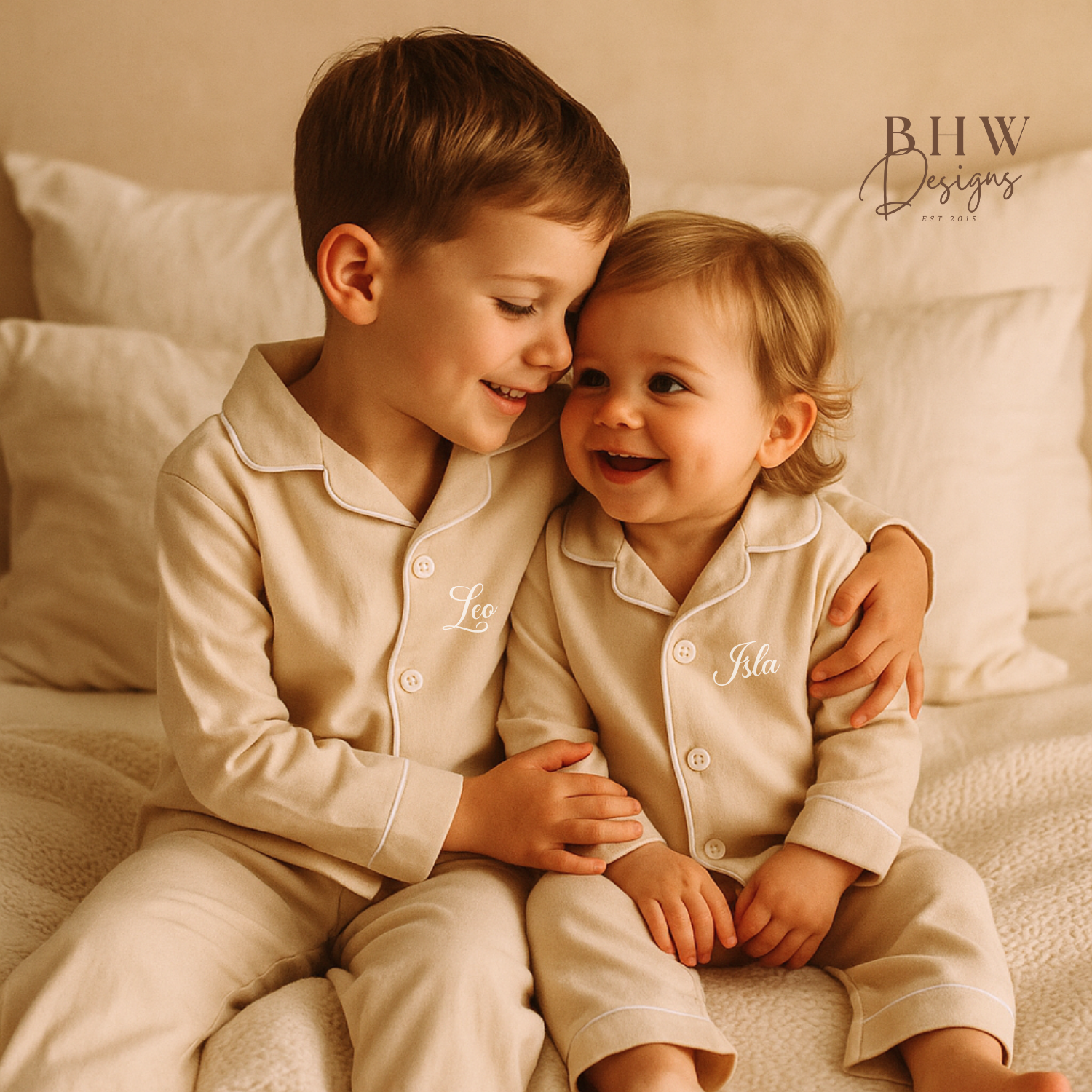 Two children in matching beige pyjamas personalised with names  sitting close together on a bed.