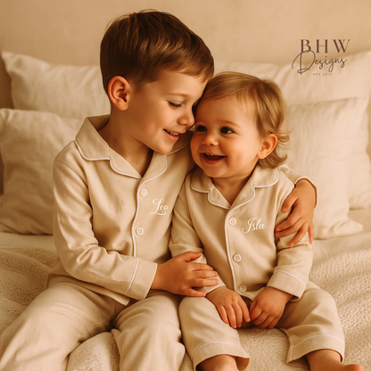 Two children in matching beige pyjamas personalised with names  sitting close together on a bed.