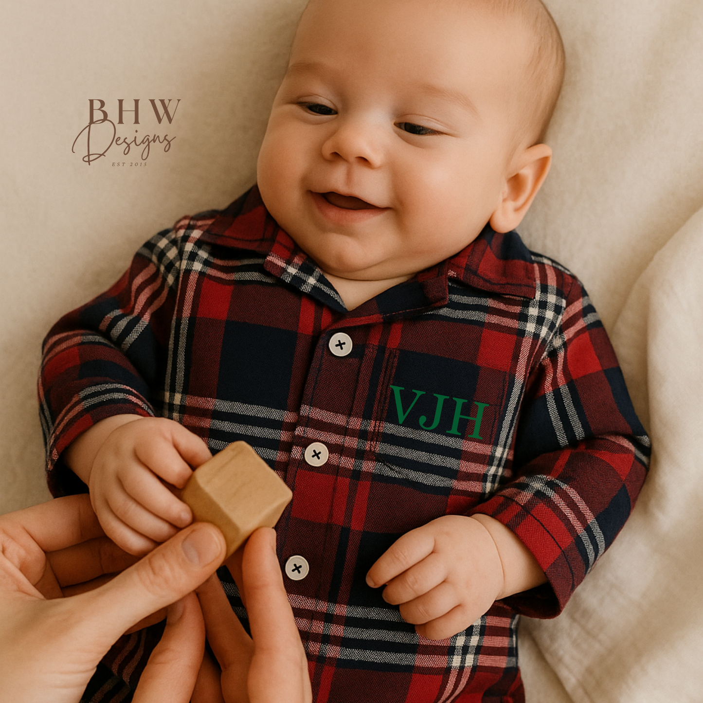 Baby wearing a red and blue plaid onesie with 'VJH' IN GREEN on the front