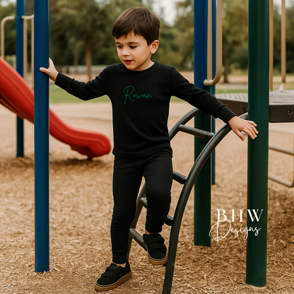 Boy wearing a black ribbed outfit with personalised Rowan on the front in Green. 