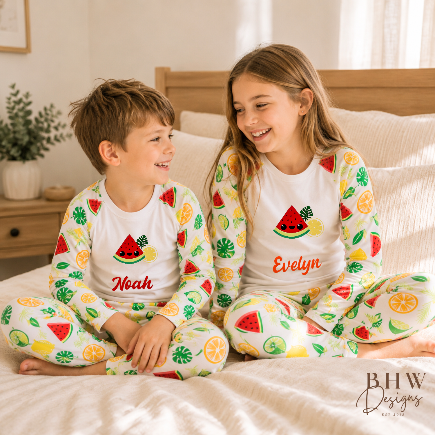 Two children in matching pyjamas with fruit patterns sitting on a bed.