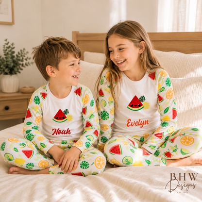 Two children in matching pyjamas with fruit patterns sitting on a bed.
