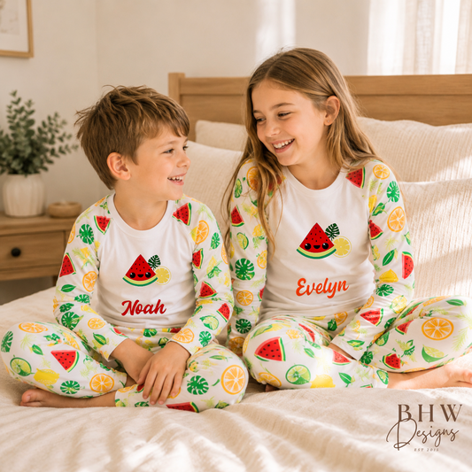 Two children in matching pyjamas with fruit patterns sitting on a bed.