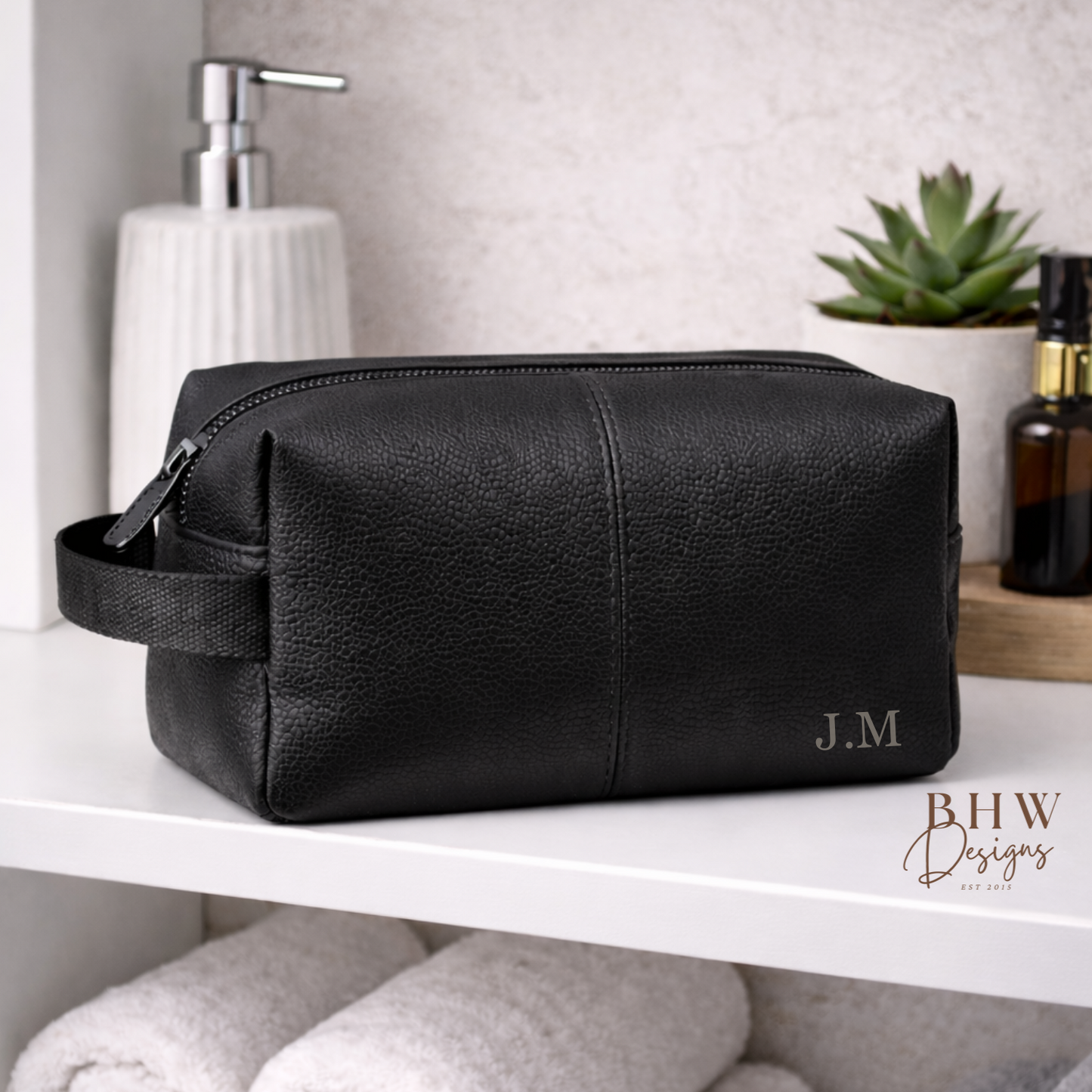 Black leather toiletry bag on a shelf with towels and a plant in the background