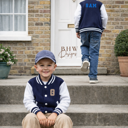 Two children wearing navy and white varsity jackets with letterman design in front of a house.