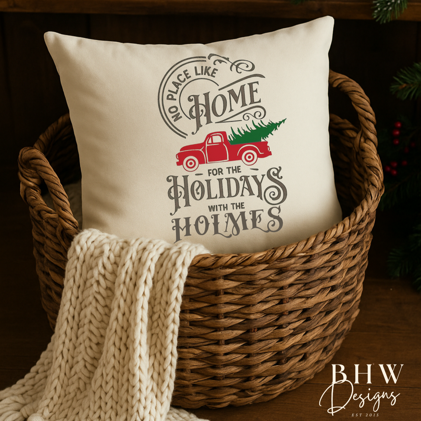 Decorative personalised family name no place like home christmas cushion in a basket with a blanket, surrounded by holiday decorations.