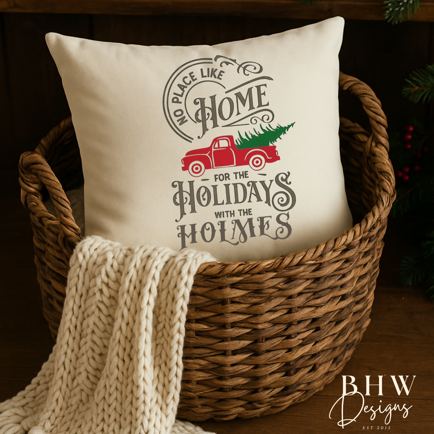 Decorative personalised family name no place like home christmas cushion in a basket with a blanket, surrounded by holiday decorations.