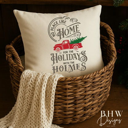 Decorative personalised family name no place like home christmas cushion in a basket with a blanket, surrounded by holiday decorations.