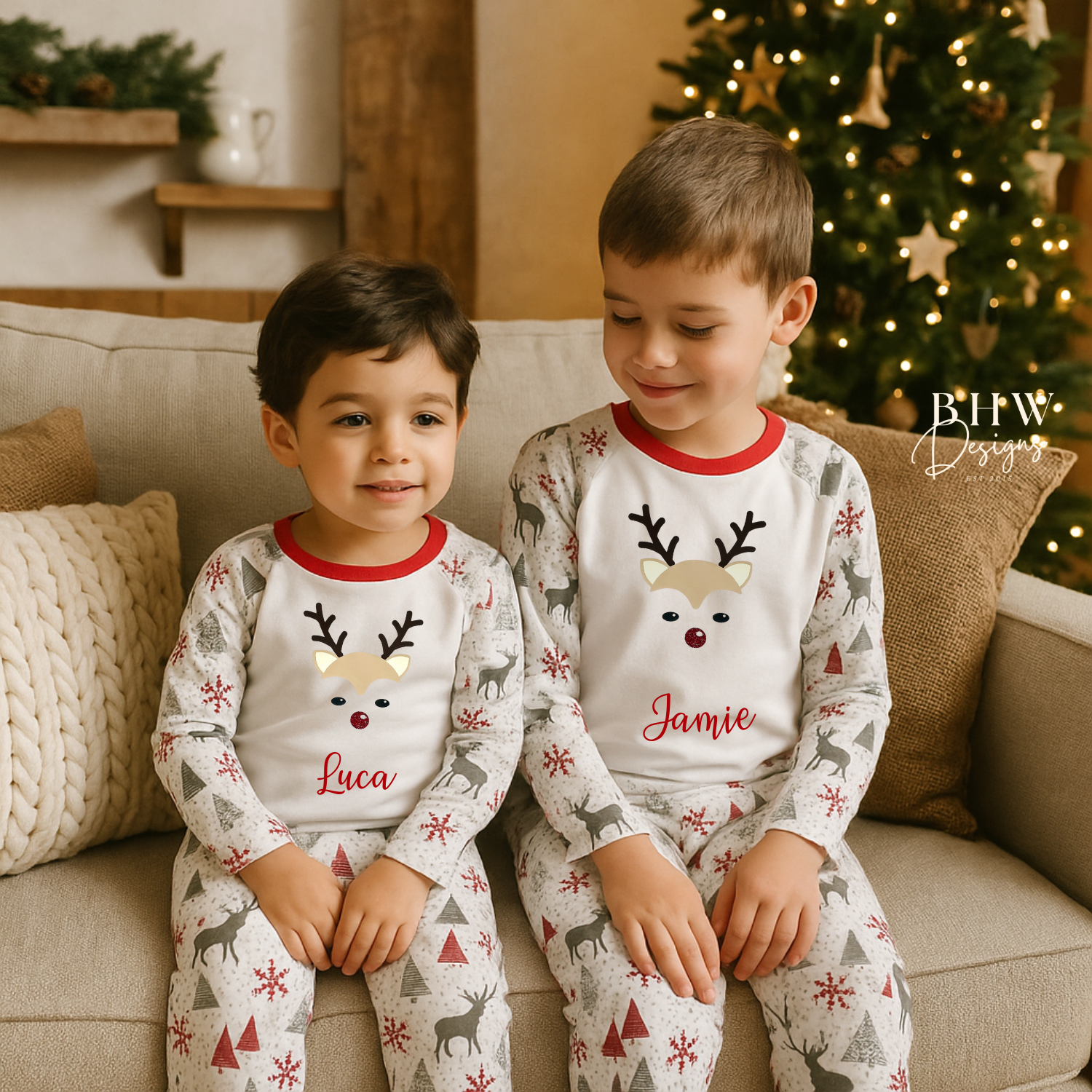 Two children wearing matching personalised pyjamas with reindeer designs sitting on a couch in a cozy living room.