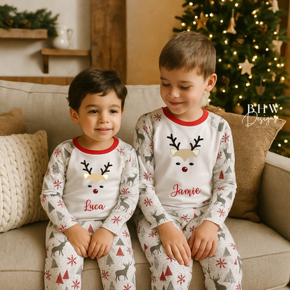 Two children wearing matching personalised pyjamas with reindeer designs sitting on a couch in a cozy living room.