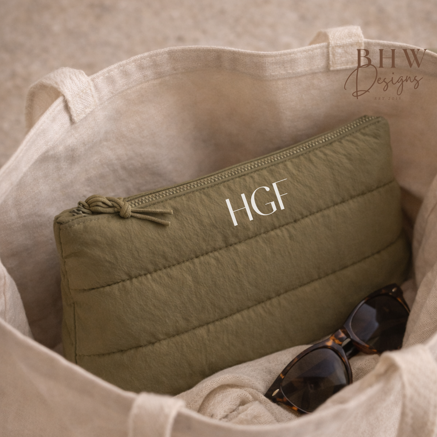 Green quilted pouch with 'HGF' monogram inside a beige bag, with sunglasses on a neutral background.